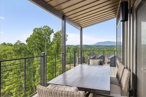 Spacious 4-bedroom cabin in Sevierville, TN, featuring a modern, rustic design with a large porch, comfortable seating area, and expansive windows. The cabin includes luxurious bedrooms, a well-equipped kitchen, a cozy living room with a fireplace, and scenic views of the surrounding mountains. The property also boasts a game room, theater room, and outdoor deck for relaxation and entertainment.