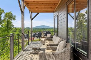 Spacious 4-bedroom cabin in Sevierville, TN, featuring a modern, rustic design with a large porch, comfortable seating area, and expansive windows. The cabin includes luxurious bedrooms, a well-equipped kitchen, a cozy living room with a fireplace, and scenic views of the surrounding mountains. The property also boasts a game room, theater room, and outdoor deck for relaxation and entertainment.